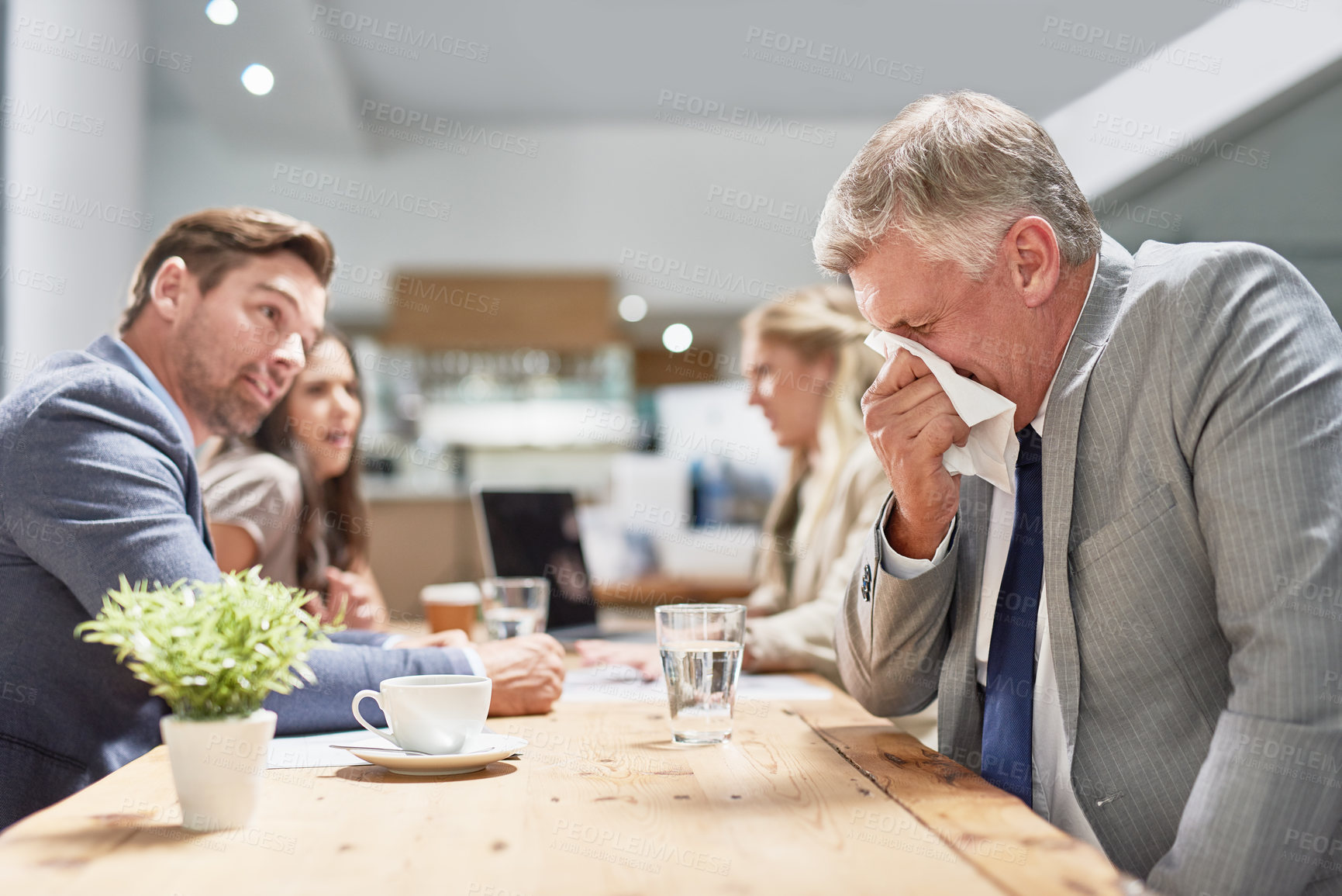 Buy stock photo Cropped shot of a businessman blowing his nose while his colleagues look on in disgust