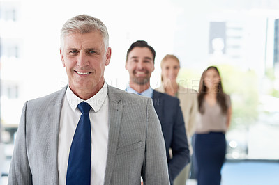 Buy stock photo Portrait of a mature businessman standing in a line with his colleagues in an office