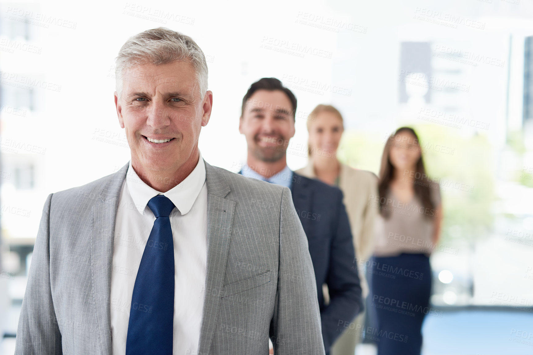Buy stock photo Portrait of a mature businessman standing in a line with his colleagues in an office