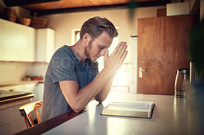 Buy stock photo Shot of a devoted young man clasping his hands in prayer over an open Bible