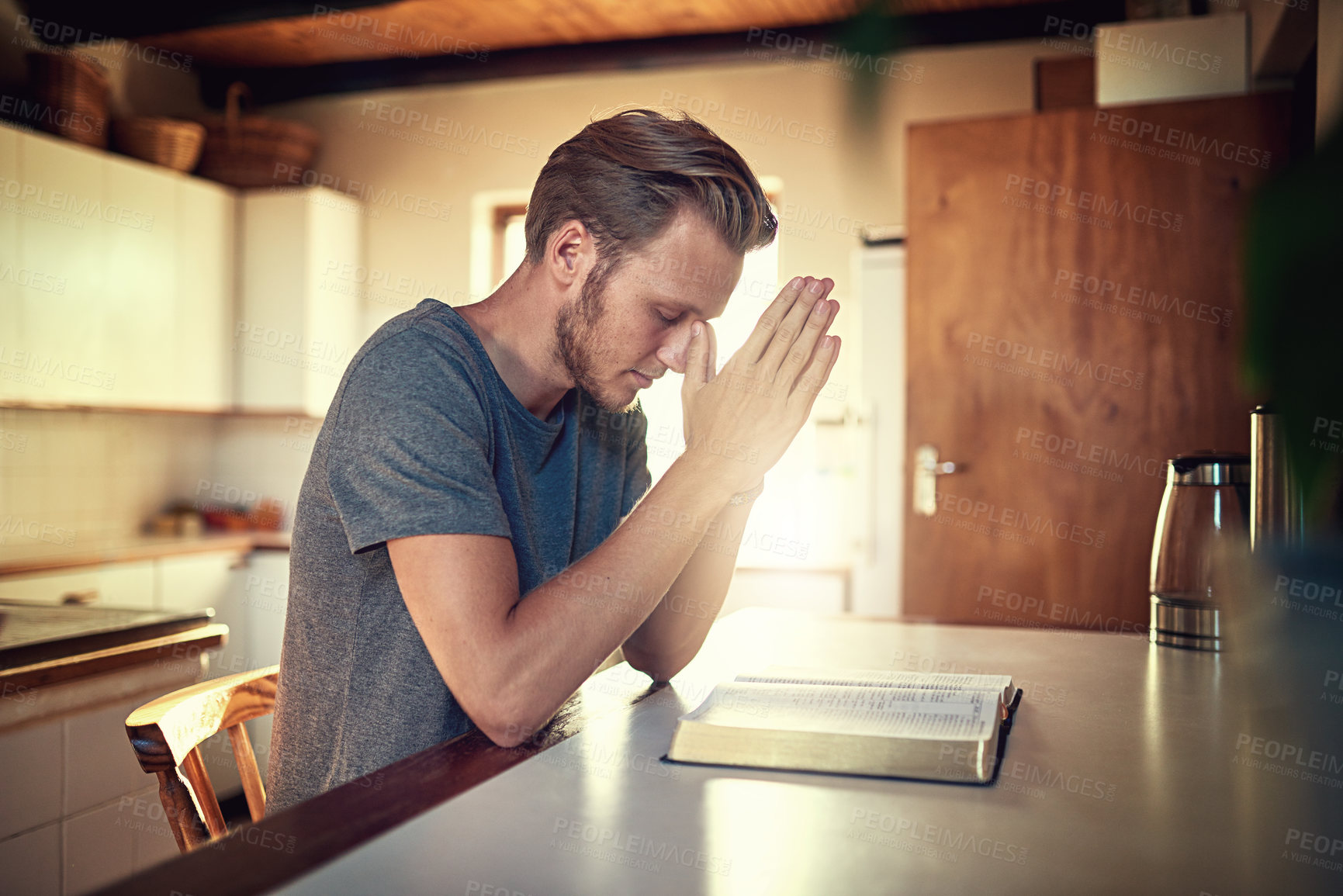 Buy stock photo Shot of a devoted young man clasping his hands in prayer over an open Bible