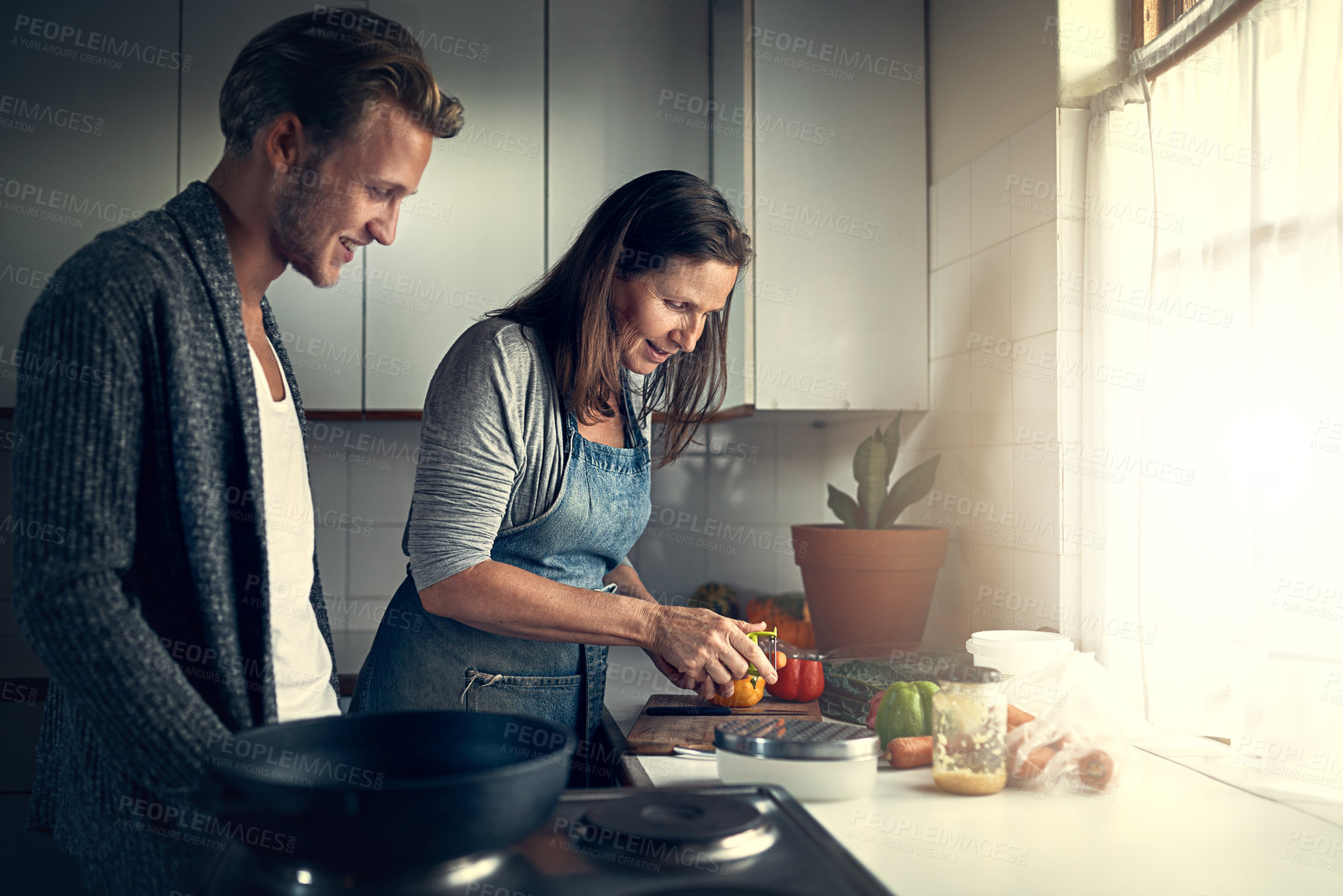 Buy stock photo Shot of a mother and her adult son cooking together in their kitchen at home