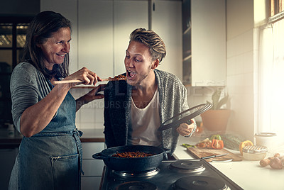 Buy stock photo Shot of mother giving her adult son a taste of what she is cooking in the kitchen