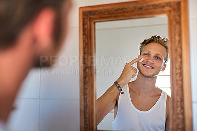 Buy stock photo Cropped shot of a young man applying moisturizer to his face
