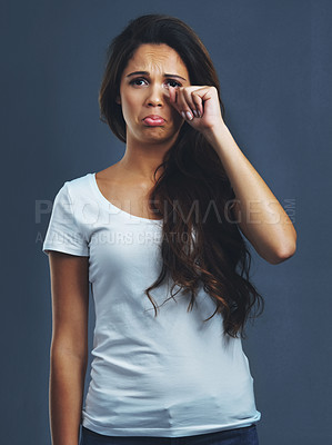 Buy stock photo Studio portrait of a young woman wiping her tears against a dark background