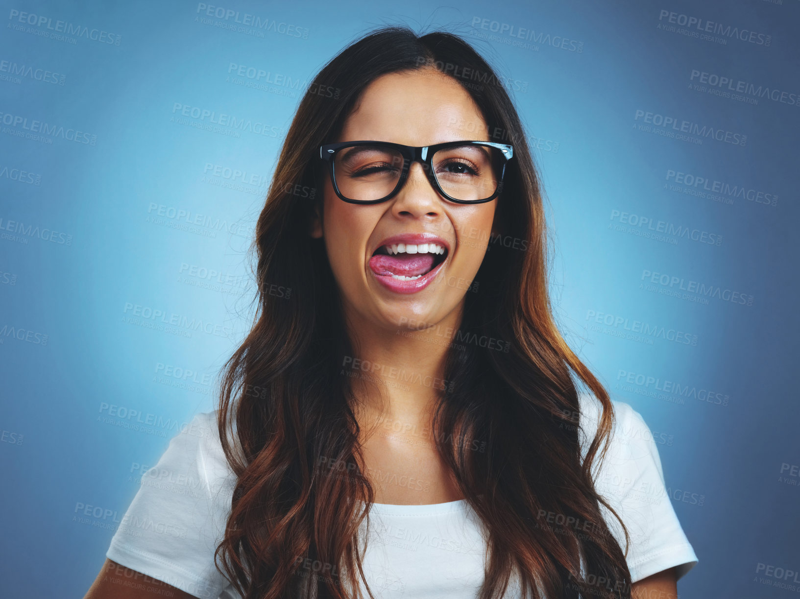 Buy stock photo Studio portrait of an attractive young woman sticking her tongue out against a blue background