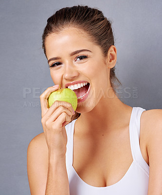 Buy stock photo Studio portrait of an attractive young woman eating an apple against a grey background