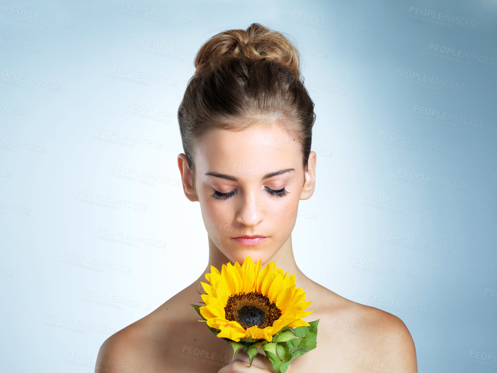 Buy stock photo Sunflower, beauty and woman in studio with natural, organic and cosmetic facial makeover. Glow, makeup and female person with yellow floral plant for cosmetology face routine by blue background.