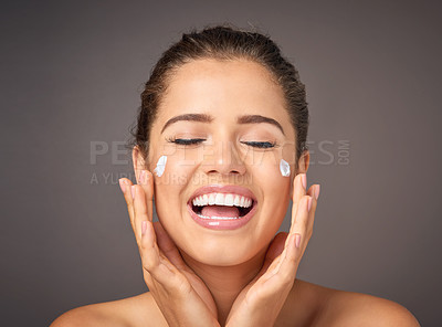 Buy stock photo Shot of a youthful model applying moisturizer to her face in studio