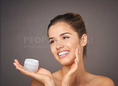 Buy stock photo Shot of a beautiful young model  holding up a tub of skin cream in studio