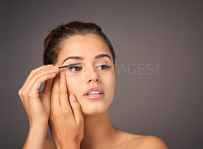 Buy stock photo Shot of a beautiful young model applying mascara to her lashes in studio