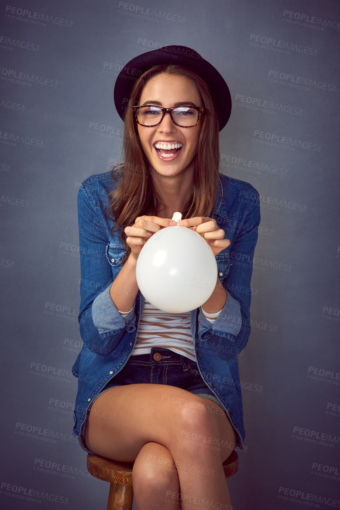 Buy stock photo Shot of a fun-loving young woman blowing up a balloon in studio