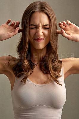 Buy stock photo Studio shot of an attractive young woman blocking her ears against a brown background