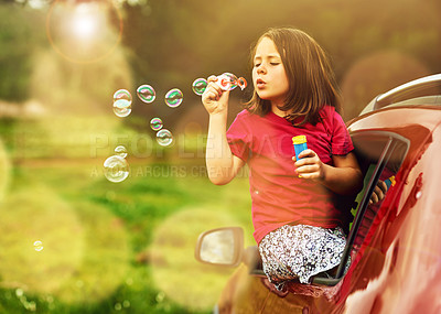 Buy stock photo Shot of a playful little girl blowing bubbles while leaning out of a car window