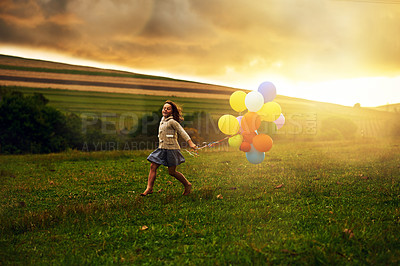 Buy stock photo Shot of a playful little girl running through a field while holding a bunch of balloons