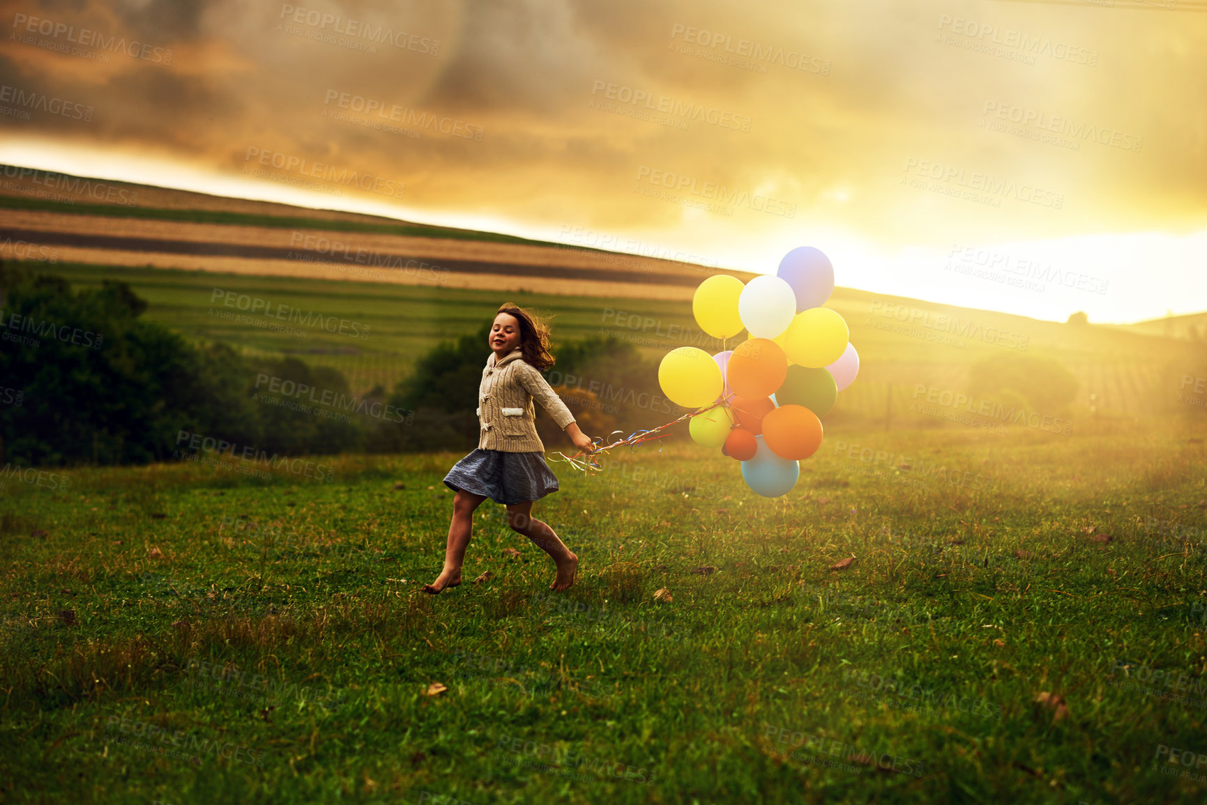 Buy stock photo Shot of a playful little girl running through a field while holding a bunch of balloons
