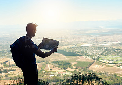 Buy stock photo Rear view shot of a young man reading a map while standing at the top of a mountain