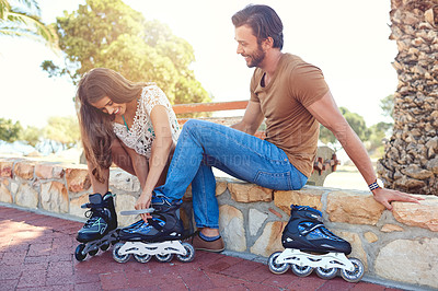 Buy stock photo Shot of a woman helping her boyfriend putting on rollerblades in a park