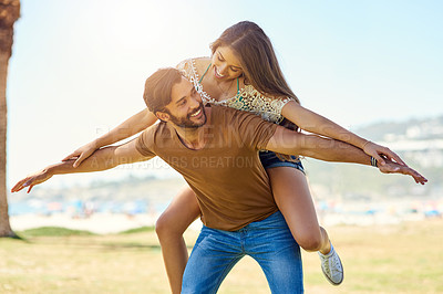 Buy stock photo Shot of a smiling young man giving his girlfriend a piggyback while enjoying a day together outside