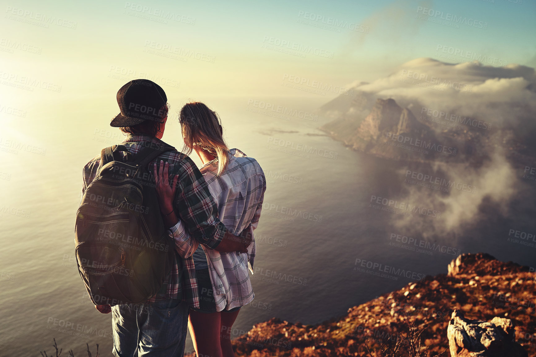 Buy stock photo Rearview shot of an unidentifiable young couple admiring the view from a mountain peak together