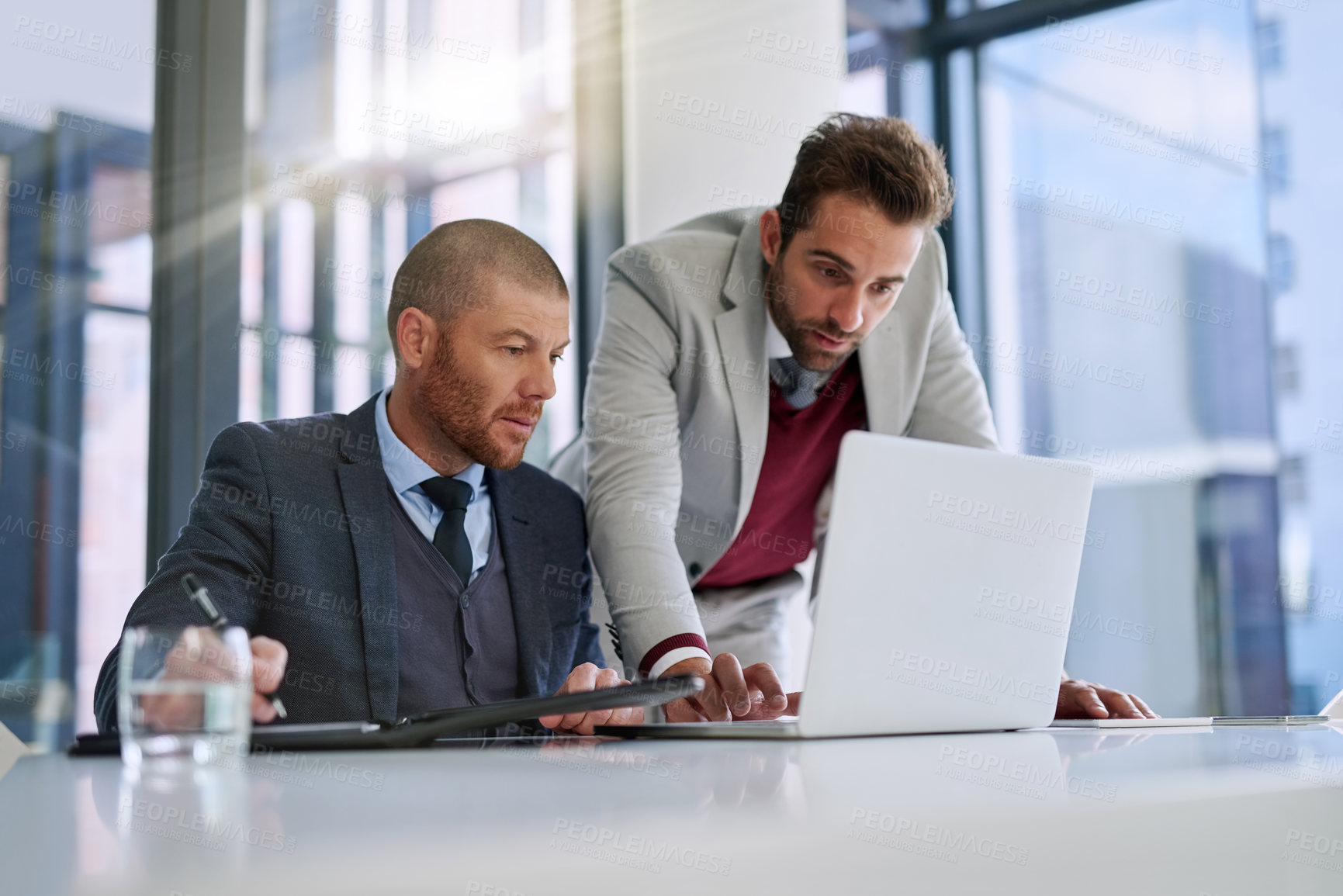 Buy stock photo Shot of two businessmen using a laptop together in a modern office