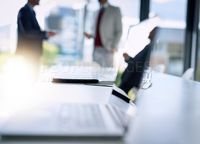 Buy stock photo Shot of an open laptop on a boardroom desk with two businessmen blurred in the background