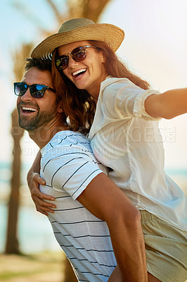 Buy stock photo Shot of a happy young couple enjoying a piggyback ride at on a summer's day outdoors