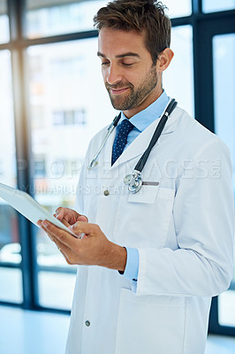 Buy stock photo Shot of a busy doctor checking a patient's medical records on his tablet