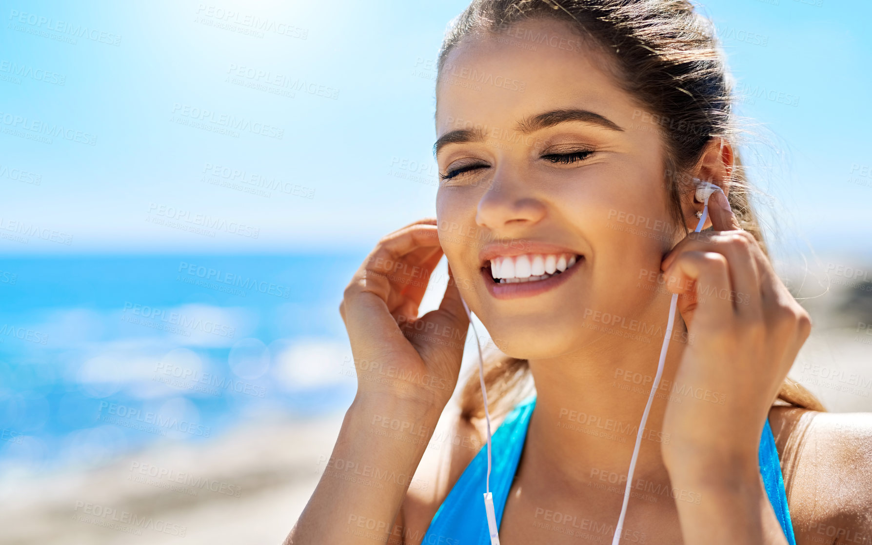 Buy stock photo Cropped shot of a young woman listening to music while out for a run by the sea