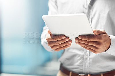 Buy stock photo Shot of an unidentifiable businessman using his tablet while standing in the office