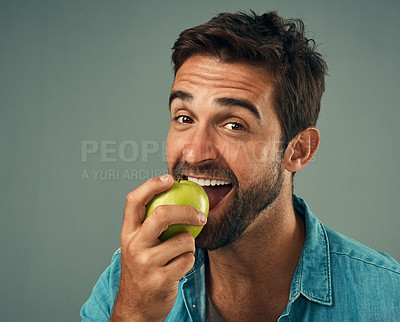 Buy stock photo Studio portrait of a handsome young man eating an apple against a grey background