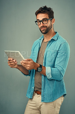 Buy stock photo Studio portrait of a handsome young man using a digital tablet against a grey background