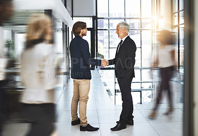 Buy stock photo Shot of two businessmen shaking hands in a busy office