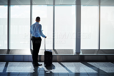 Buy stock photo Shot of a businessman looking through airport windows and using a cellphone while on a business trip