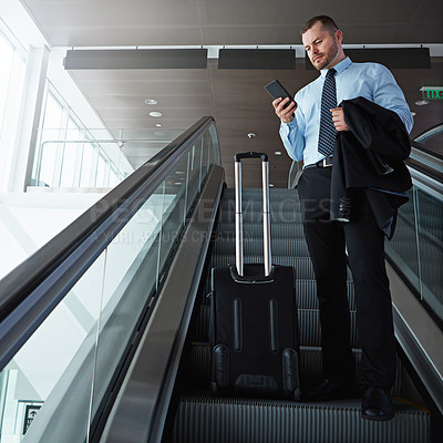 Buy stock photo Shot of a businessman using a mobile phone while traveling down an escalator in an airport