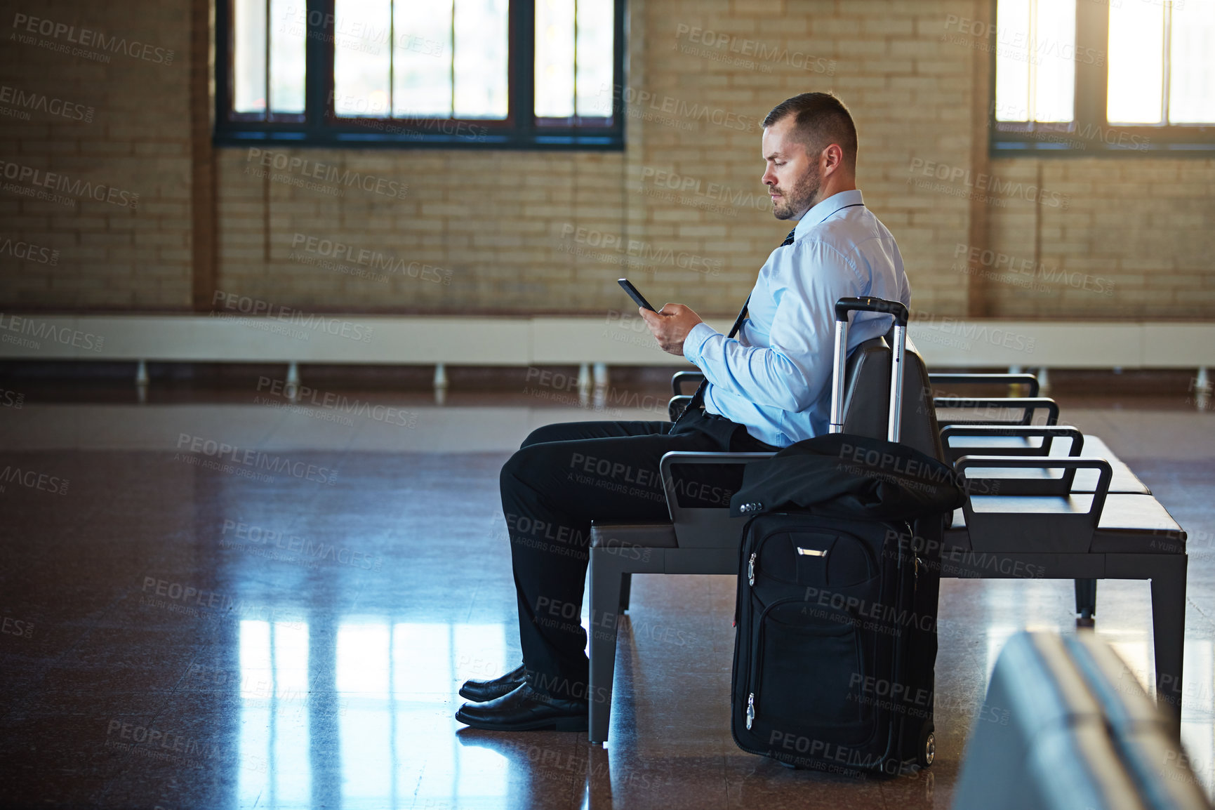 Buy stock photo Shot of a confident businessman using his smartphone while waiting in an airport terminal