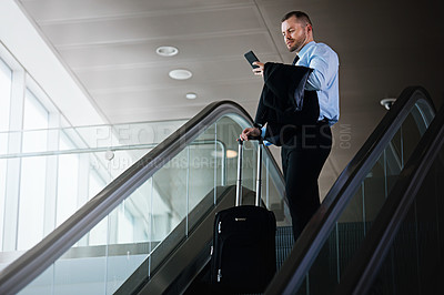 Buy stock photo Shot of a businessman using a mobile phone while traveling down an escalator in an airport