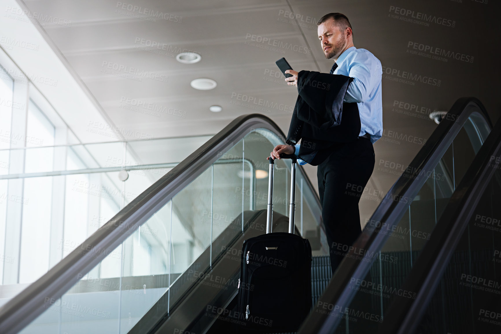 Buy stock photo Shot of a businessman using a mobile phone while traveling down an escalator in an airport