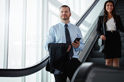 Buy stock photo Shot of a businessman and businesswoman traveling down an escalator in an airport