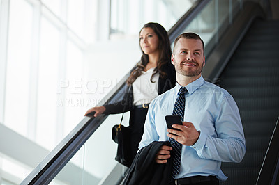 Buy stock photo Shot of a businessman and businesswoman traveling down an escalator in an airport