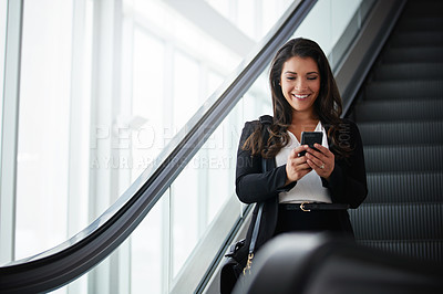 Buy stock photo Shot of a businesswoman using a mobile phone while traveling down an escalator in an airport