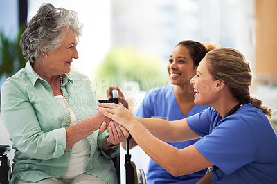 Buy stock photo Shot of a smiling female doctor and nurse talking with a senior woman in a wheelchair