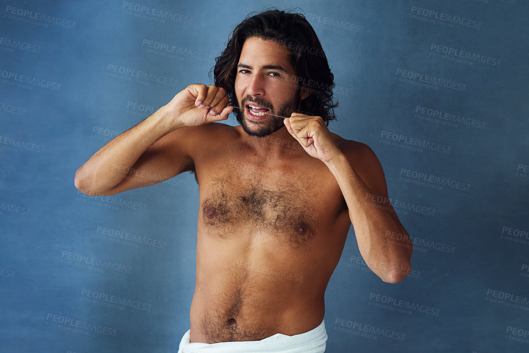 Buy stock photo Studio portrait of a handsome young man flossing his teeth against a blue background