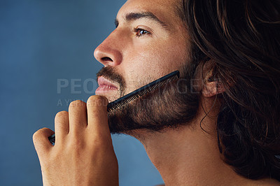 Buy stock photo Studio shot of a handsome young man grooming his facial hair against a blue background