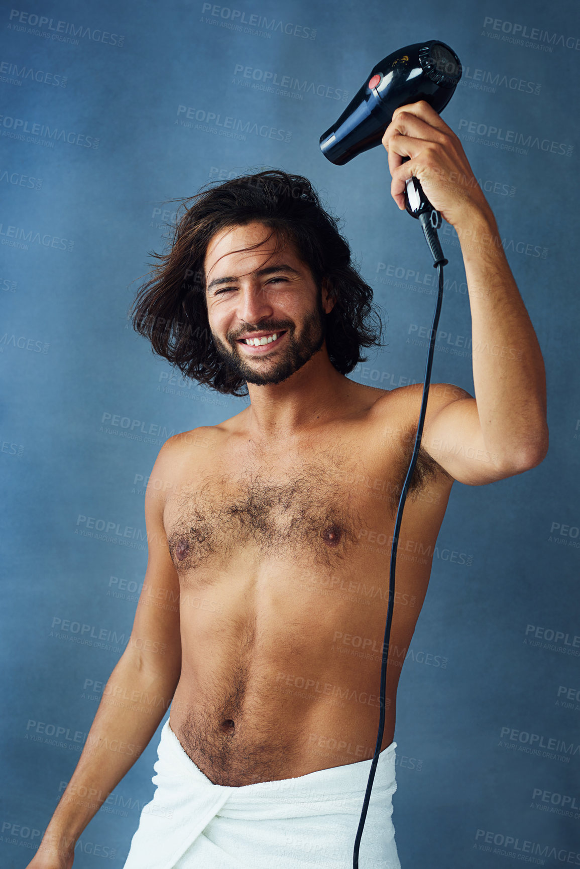 Buy stock photo Studio portrait of a handsome young man blowdrying his hair against a blue background