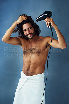 Buy stock photo Studio portrait of a handsome young man blowdrying his hair against a blue background