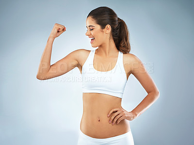 Buy stock photo Studio shot of an attractive young woman flexing her muscles against a grey background