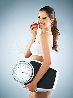 Buy stock photo Studio portrait of an attractive young woman holding an apple and a scale against a grey background