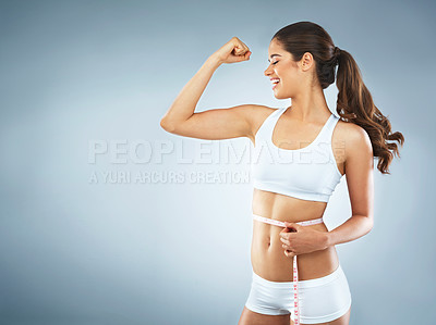Buy stock photo Studio shot of an attractive young woman flexing her muscles while measuring her waist against a grey background
