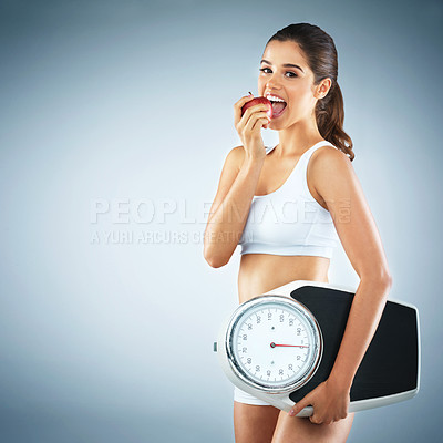 Buy stock photo Studio portrait of an attractive young woman holding an apple and a scale against a grey background
